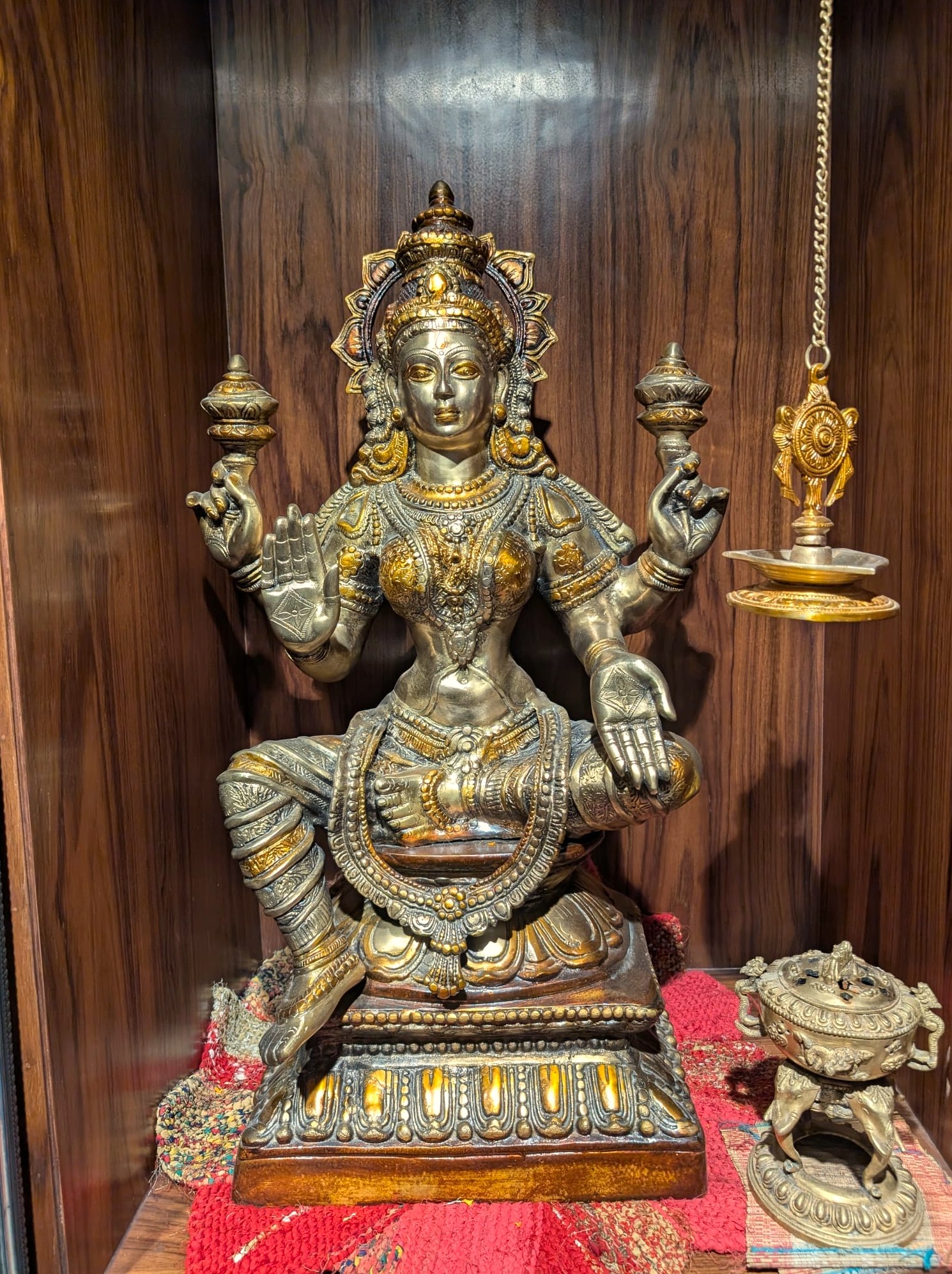 The brass Lakshmi statue in the teak alcove, with a hanging diya and incense burner